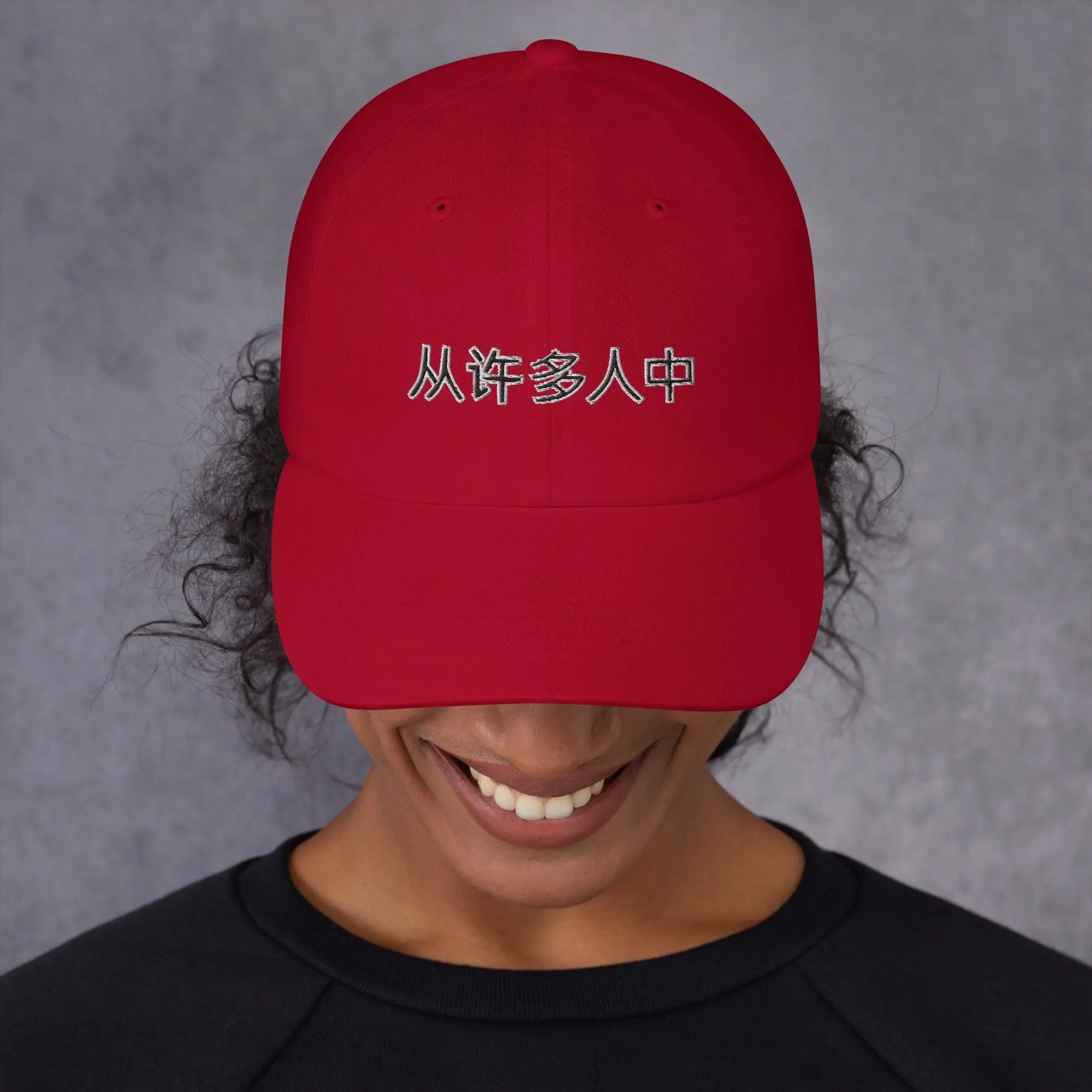 Red unisex hat with embroidered Chinese phrase "Out Of Many One People" worn by smiling person